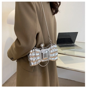 Detail of silver bow-shaped clutch with metallic finish and large pearl clasp on the shoulder