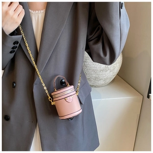 Detail of pink mini cylinder bucket bag with gold chain strap on a grey suit jacket