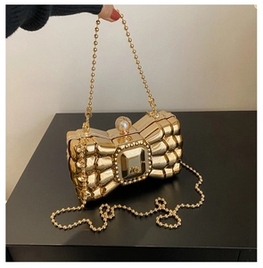 Close-up of golden bow-shaped evening bag with textured metallic finish and pearl clasp