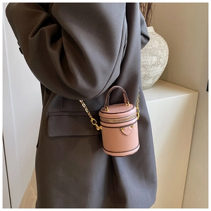 Close-up of a mini pink textured leather bucket bag with gold chain strap on a model