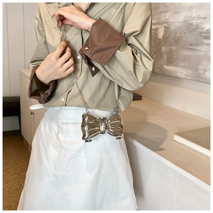 Silver bow-shaped metallic evening bag worn by model over a brown shirt and white skirt