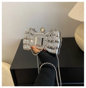 Detail of silver bow evening clutch with pearl clasp, mirror finish and bead chain