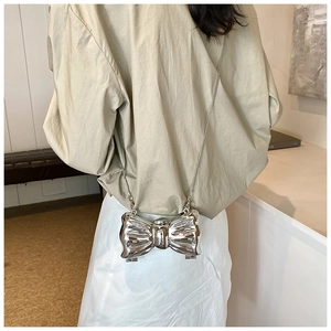 Silver mirror butterfly bow bag with metal chain strap worn by a model in interior