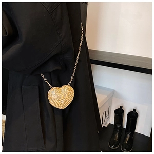 Detail of a sparkling heart shaped mini bag with golden chain on a black coat outfit