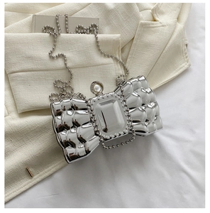 Detailed view of silver bow clutch bag with crystal buckle and pearl clasp on fabric