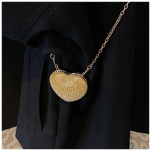 Sparkling heart-shaped clutch bag with gold crystals and fine metal chain on dark coat