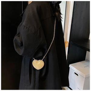 Close-up of heart-shaped gold evening bag with rhinestones and chain strap on a black coat