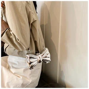 Detail of silver metallic bow-shaped bag with reflective mirror finish and chain strap