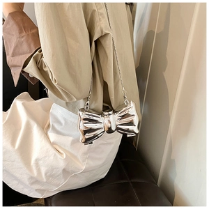 Detailed view of silver metallic bow-shaped clutch with mirror finish and long chain strap