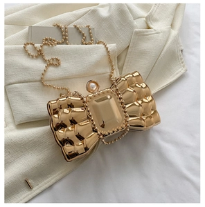 Detail of gold bow-shaped clutch featuring a faceted crystal and pearl clasp with chain