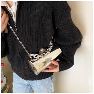 Detail of silver cylindrical clutch featuring pearl clasp and metallic chain strap