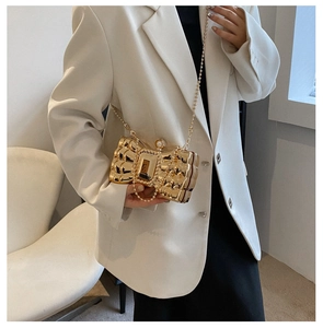 Detail of gold bow evening clutch with pearl clasp and chain on a white blazer