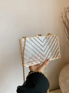 Detail of transparent acrylic clutch bag with V-shaped texture and gold metal chain