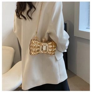 Detailed side view of a gold bow evening clutch bag with pearl clasp and chain strap