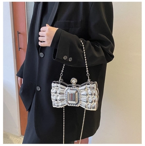 Macro shot of silver bow clutch with crystal stone and pearl clasp worn over black suit