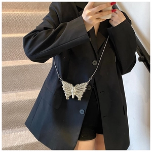 Mini sac papillon argenté avec chaîne porté par un mannequin sur un escalier beige