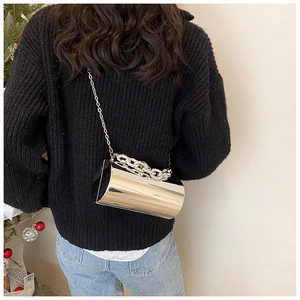 Detail of a shiny gold cylinder bucket bag featuring a thick chain handle and metal strap