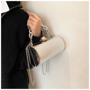 Detail of glossy bucket bag with pearl clasp and metal chain strap on model