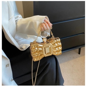 Detail of golden bow clutch featuring pleated metallic finish and pearl clasp closure