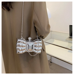 Silver bow-shaped evening clutch with pearl clasp and chain strap on a model