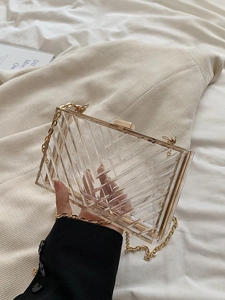 Detailed view of clear acrylic handbag featuring golden metal frame and chevron texture