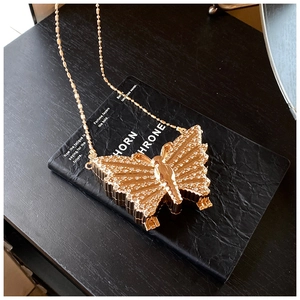 Détail d'une pochette papillon dorée ornée de strass et d'une bandoulière en chaîne