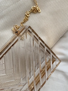 Detail of transparent acrylic box bag with geometric cut texture and gold chain strap
