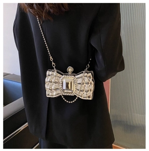 Detail of silver butterfly-shaped clutch with crystal stone and pearl top on black suit