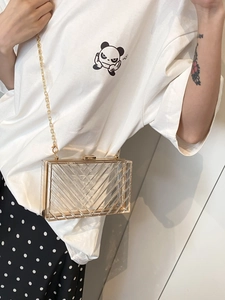 Close-up of transparent acrylic box bag with gold metal trim and V-shaped stripe texture