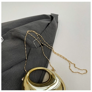 Close-up of golden acrylic clutch bag with round top handle and beaded chain strap