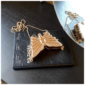 Détail d'une pochette papillon dorée avec strass scintillants et chaîne fine