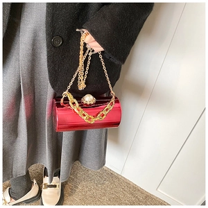 Chic red cylindrical evening bag with gold chain and large pearl clasp detail