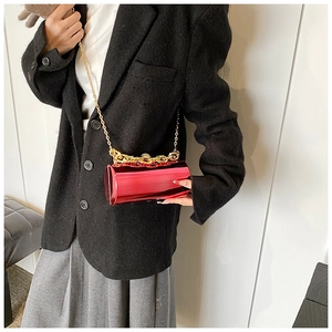 Macro detail of wine red cylindrical evening bag with glossy mirror finish and gold chains