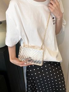 Detail of transparent acrylic clutch bag with V-shaped texture and gold metal chain strap