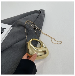 Detailed close-up of a golden pebble-shaped acrylic clutch bag with shiny mirror finish