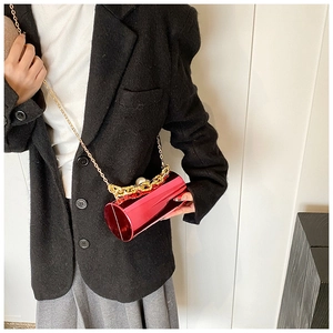 Close-up of red patent bucket bag with golden chain and pearl detail on black blazer
