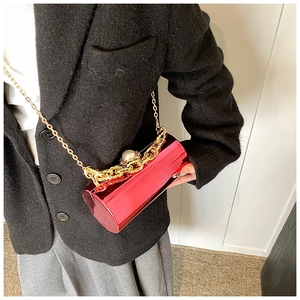 Metallic red cylindrical evening bag with gold chain and pearl on a black suit jacket