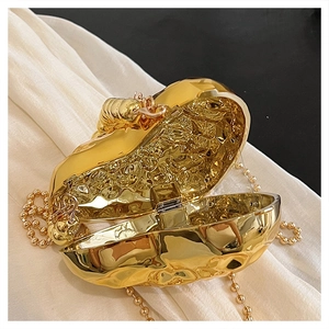 Dettaglio della pochette cuore dorata con chiusura a insetto, trama martellata e catena