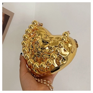Dettaglio di una borsa da sera a cuore dorata con texture metalliche ondulate e catena a sfere