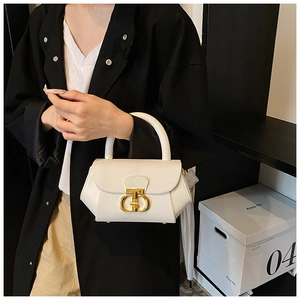 Close-up of white lychee leather handbag with golden metal buckle and curved handle