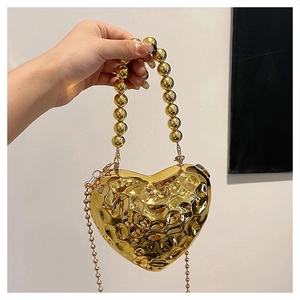 Dettaglio della borsa a cuore dorata con trama martellata e manico di perle