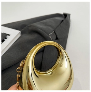 Macro shot of mirror-polished gold metal drop clutch bag with round cutout handle