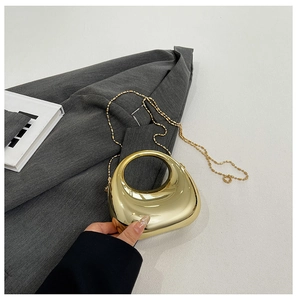 Close-up of golden crescent acrylic clutch with glossy mirror finish and ball chain strap