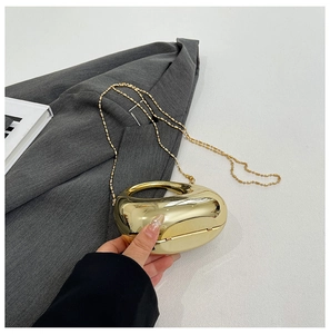 Close-up of golden bean-shaped acrylic clutch bag with round handle and bead chain on suit