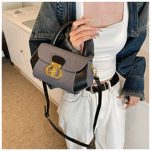 Detail of grey fabric bag with black leather flap and golden CD buckle on denim jacket