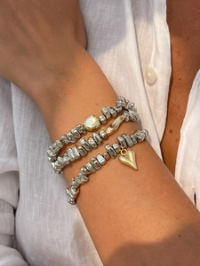 Gros plan de bracelets en perles d'argent avec charms cœur dorés sur du lin blanc