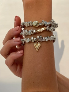 Détail de bracelets en perles d'argent superposés avec charms coeur dorés au poignet