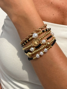 Détail de bracelets superposés en perles dorées et noires avec pendentif pièce et perles