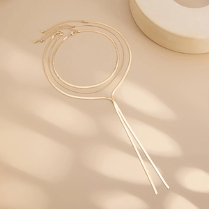 Detailed view of layered gold snake bone chain necklaces on warm beige background