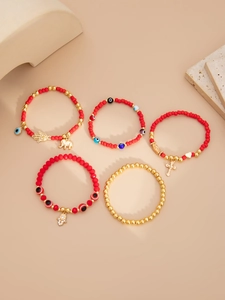 Détail de bracelets en perles rouges et dorées avec breloques Hamsa et Evil Eye